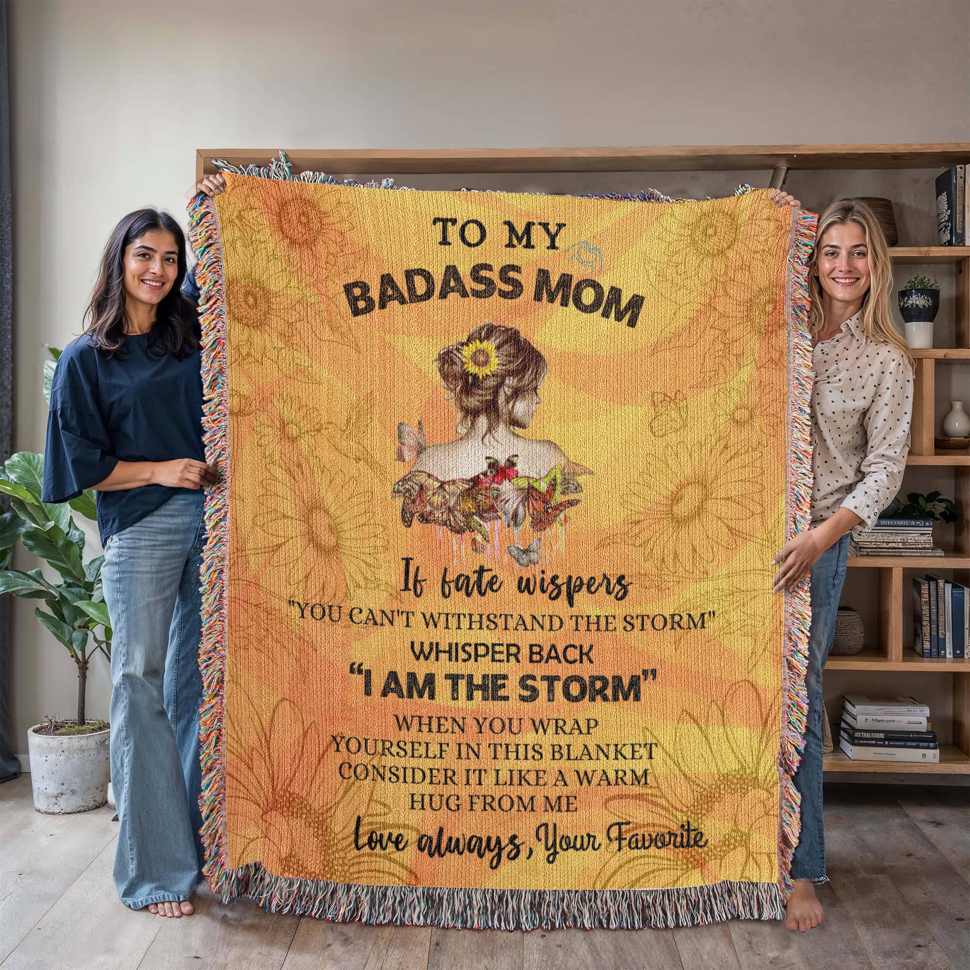 Personalized wooven blanket with sunflower design and "To My Badass Mom" message. Held up by 2 women