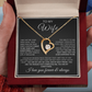 Gold heart-shaped necklace with a message card for 'To My Wife' held in hands.